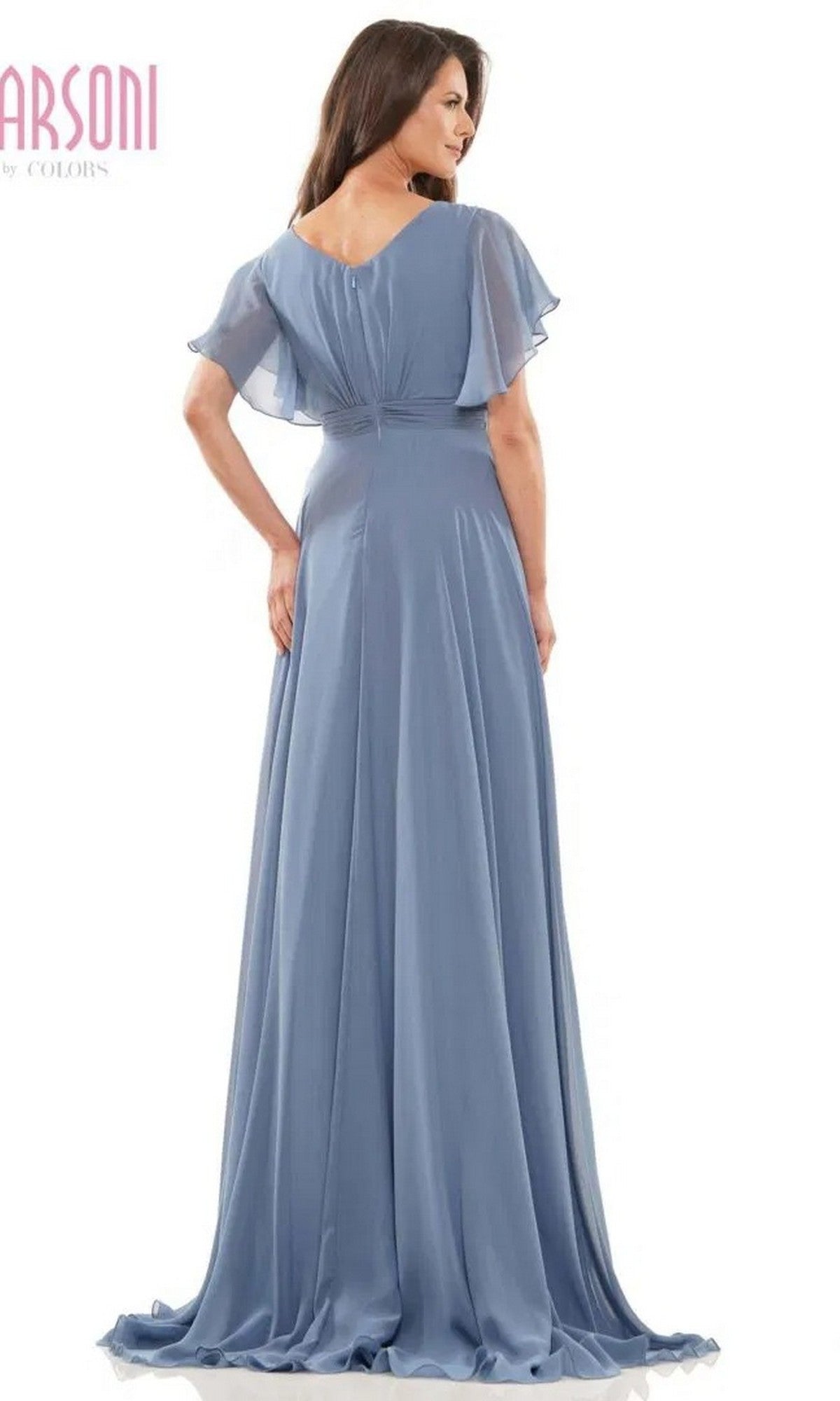 A woman stands with her back to the camera, wearing the Marsoni M320 long formal dress—a floor-length, light blue chiffon gown with an a-line skirt and short flutter sleeves.